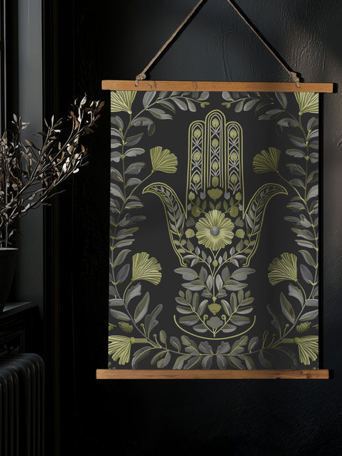 Botanical Hamsa wall tapestry featuring intricate sage green and lavender design on black background, showing a protective hand symbol surrounded by leaf motifs and floral elements, hanging from wooden dowels with natural twine.